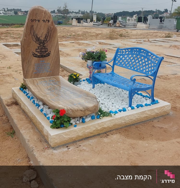 מצבה עם אבן גדולה, ספסל כחול ופרחים